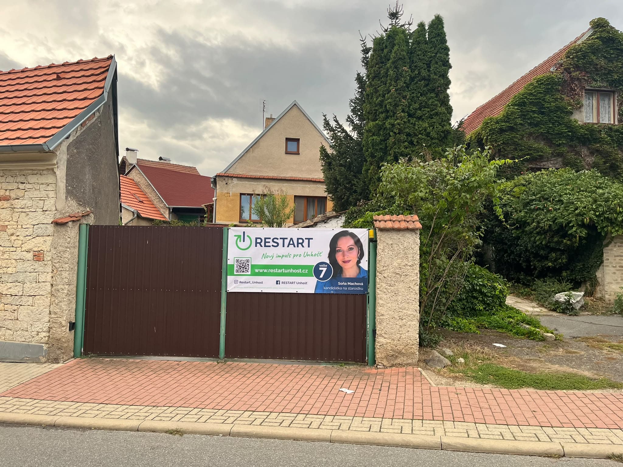 Plachta RESTARTu pověšená na vratech domu v ulici Na Hrádku mezi starou zástavbou Unhoště