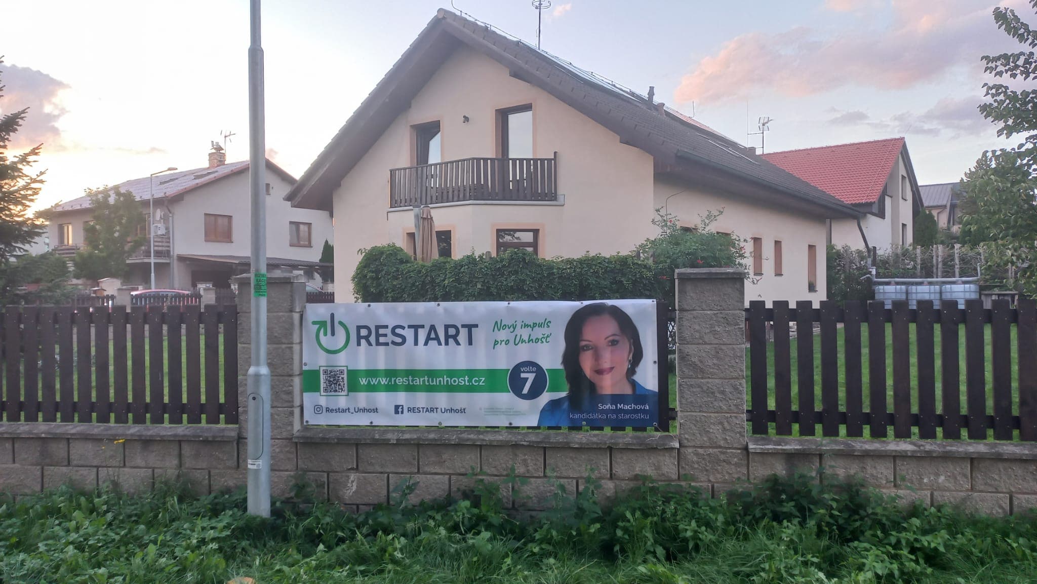 Plachta RESTARTu na plotě rodinného domu v Unhošti v podvečerním světle